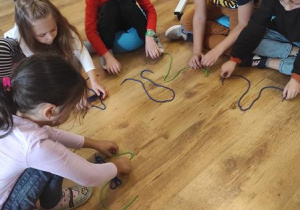 Dzieci układają kształt wielkiej i małej litery A ze sznurka.